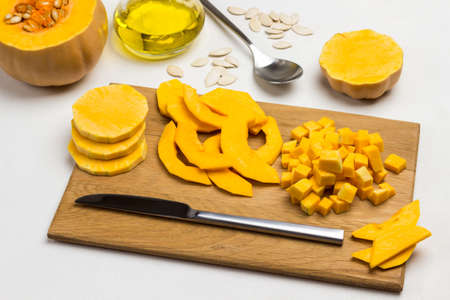 Chopped pumpkin pieces and knife on cutting board. Pumpkin with seeds. Oil, seeds and spoon on table. Top view. White backgroundの写真素材