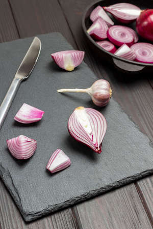Chopped onion and knife on cutting board. Sliced purple onions in bowl. Dark wooden background. Top viewの写真素材