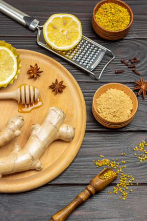 Ginger root, lemon and star anise on cutting board. Lemon on grater. Dry ginger in bowl. Pollen in scoop. Dark wooden background. Top viewの写真素材