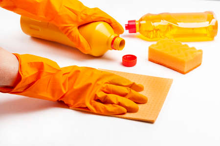 Orange rubber gloves hold orange rag and orange plastic bottle. White background.の写真素材