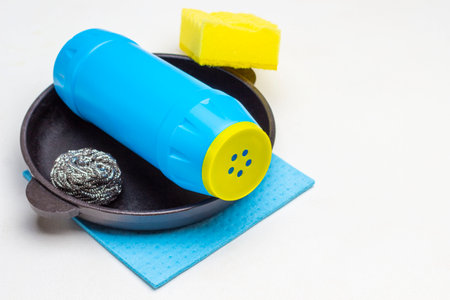 Cast iron pan, scouring powder and scrub buds. Yellow sponge and blue rag. Copy space. White background. Top viewの写真素材