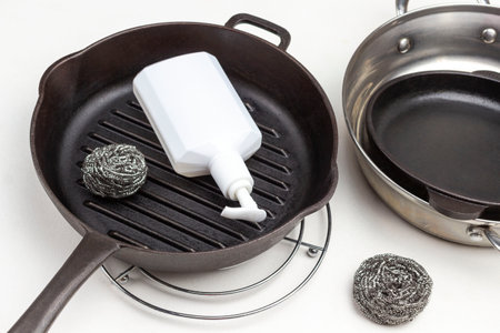 White plastic bottle and scrub buds in frying pan, several frying pans. White background. Top viewの写真素材