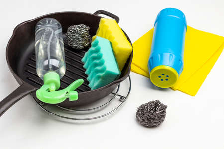 Spray bottle, sponges and scrub buds in frying pan. Blue plastic bottle with cleaning powder on yellow rag. White background. Top viewの写真素材