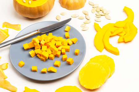 Small pieces of pumpkin and knife on gray plate. Sliced pumpkin and seeds on table. White background. Top view.の写真素材