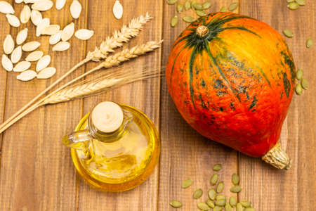 Orange pumpkin and bottle of oil. Dry wheat sprigs and pumpkin seeds. Flat lay. Wooden background.の写真素材