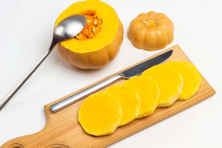 Sliced pumpkin and knife on cutting board. Spoon in pumpkin pulp. White background. Top view.の写真素材