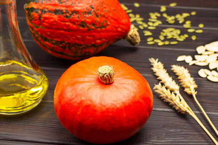 Ripe orange pumpkins and dry wheat sprigs. Bottle of oil and pumpkin seeds. Dark wooden background. Top viewの写真素材