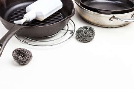 White plastic bottle in frying pan. Several frying pans and scrub buds on table. Copy space. White background. Top viewの写真素材