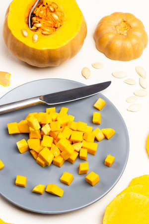 Small pieces of pumpkin and knife on gray plate. Spoon in pumpkin pulp. Sliced pumpkin and seeds on table. White background. Top view.の写真素材