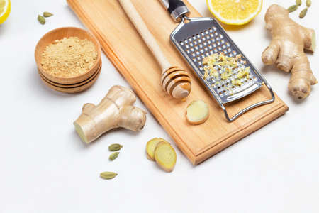 Grater with grated ginger. Stick with honey on board. Ginger root, dry ginger and lemon on table. White background. Top viewの写真素材