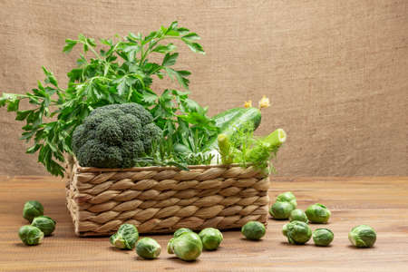 Broccoli, fennel, parsley branches in a wicker basket. Brussels sprouts on the table. Copy space. Wooden background.の写真素材