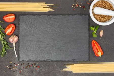 Spaghetti, chopped tomatoes and peppers. Coriander seeds in mortar. Allspice on table. Black board. Food Menu concept. Black background. Flat lay.の写真素材
