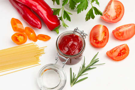 Tomato sauce in glass jar. Tomato slices, peppers and pasta on table. White background. Flat layの写真素材