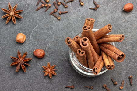Cinnamon sticks in glass jar. Star anise, cloves and nuts on table. Flat lay. Black background.の写真素材