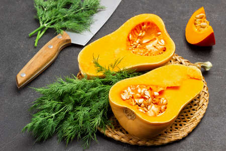Pumpkin halves and bunch of dill on wicker plate. Dill and kitchen knife on table. Top view. Black backgroundの写真素材