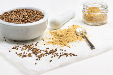 Coriander seeds in porcelain mortar. Ground ginger in jar and on paper. Pestle, coriander and dry ground ginger. White background. Top view.の写真素材