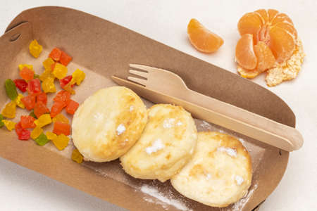 Cottage cheese pancakes in disposable plate, fork and knife. Mandarin on table. White background. Top viewの写真素材