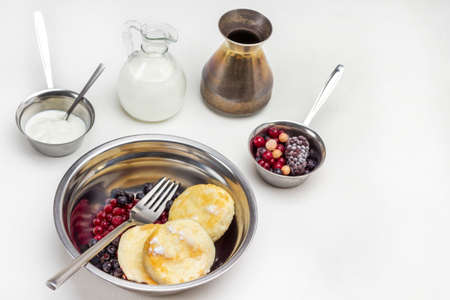 Berries, fork and cottage cheese pancakes and berries in metal bowl. Frozen berries and yoghurt in small metal bowl. Milk in glass bottle. White background. Top view.の写真素材