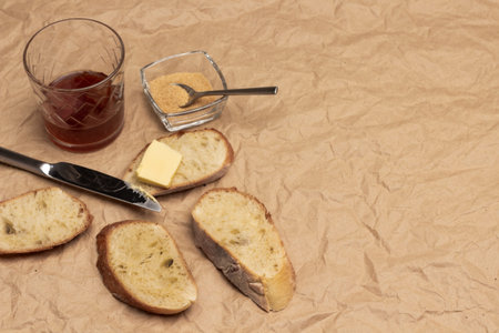 Butter and knife on slice of loaf. Sugar and glass of tea. Copy space. Flat lay. Brown paper...