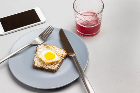 Fork and knife, toast with grated cheese and boiled quail eggs on gray plate. Fruit drink in glass...