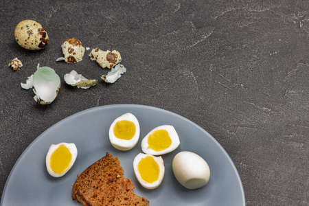 Boiled egg halves and toast on gray plate. Quail eggshells on table. Copy space. Black background. Flat layの写真素材