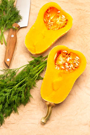 Halves of pumpkin, dill sprigs and knife on brown paper. Top view.の写真素材