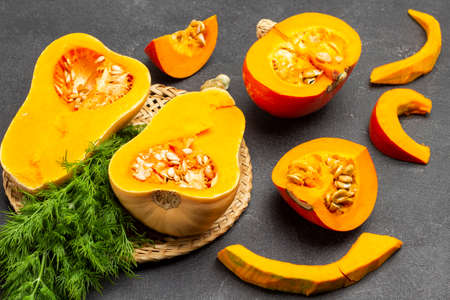 Two halves of pumpkin and dill on wicker plate. Sliced pumpkin on table. Top view. Black backgroundの写真素材