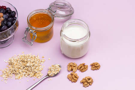 Honey and yogurt in glass jars. Oatmeal and nuts on the table. Copy space. Top view. Pink backgroundの写真素材