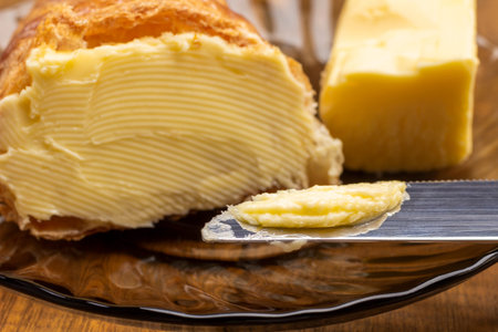 Butter on knife and on croissant. Piece of butter on saucer. Close up