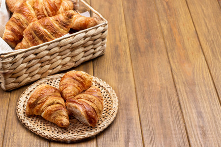 Fresh croissants in wicker basket and plate. Copy space. Top view. Wooden background.