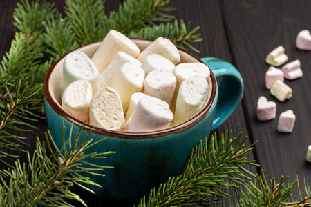 Marshmallows in ceramic mug among pine branches. Top view. Dark wooden background ..の写真素材