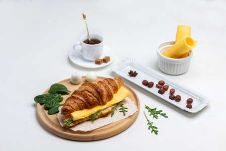 Breakfast. Croissant with cheese and greens. Nuts on plate. Cup of coffee. Top view. White background.の写真素材