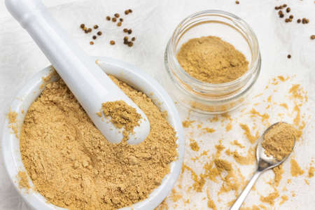 Ground ginger in mortar and pestle. Dry ground ginger in jar and on table. Flat lay. White background.の写真素材