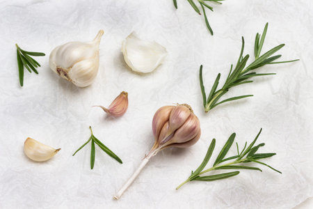 Heads of garlic and rosemary sprigs on paper. Flat lay. White background.