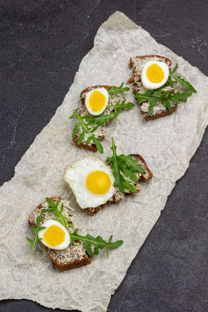 Sandwiches with boiled eggs, arugula and grated cheese on paper. Top view. Black background.の写真素材
