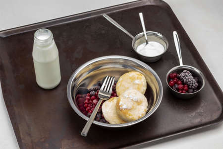 Cheesecakes with frozen berries and fork in metal plate. Cream in glass bottle. Berries and yogurt in bowls. Rusty metal pallet.の写真素材