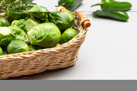Brussels sprouts in wicker basket. Fresh green peppers on table. white backgroundの写真素材