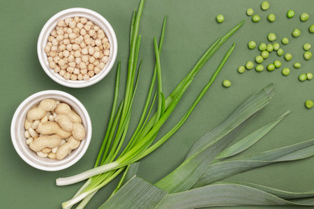 Chickpeas and nuts in white bowls. Leek, green pea and scallion. flat lay. green background.の写真素材