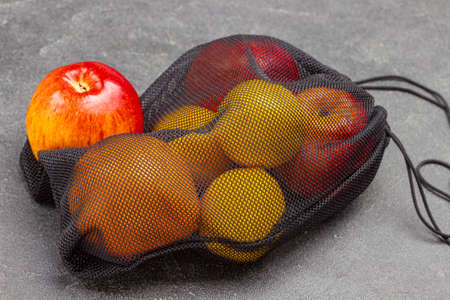 Apple on reusable string bag with fruits. top view. Black background.の写真素材