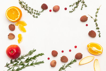 fruit still life. Lychee berries, apple, orange halves and sprigs of thyme around edges of...