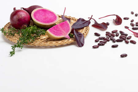 Pink radish halves and purple onions on wicker plate. bean seeds. copyspace. white backgroundの写真素材