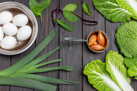 Eggs in metal bowl, leeks and shallots, spinach leaves and savoy cabbage. flat lay. wooden background.の写真素材