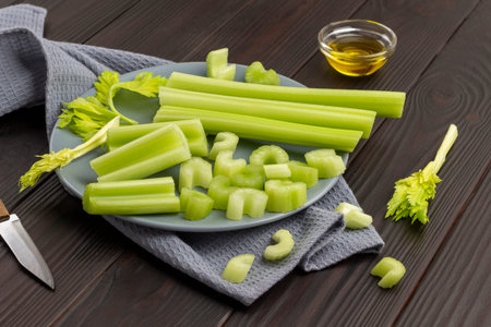 Chopped celery stalks on gray plate on napkin. Knife and olive oil in bowl. top view. wooden...