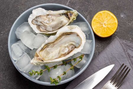 Oysters with ice in bowl. Lemon knife and fork on table. flat lay. black backgroundの写真素材