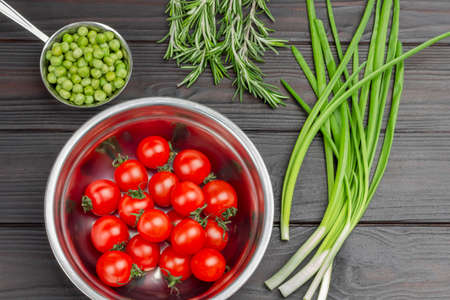 Tomatoes and fresh green peas in metal bowls. Green onions and rosemary. flat lay. dark wooden backgroundの写真素材