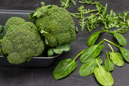 Broccoli in metal baking dish. Spinach leaves and arugula. top view. Black background.の写真素材