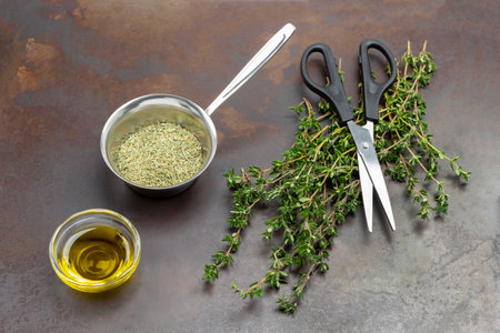 Sprigs of green thyme and dry thyme in metal bowl. Oil in glass bowl. Scissors on sprigs of thyme. Top view. Rusty metal background.の写真素材
