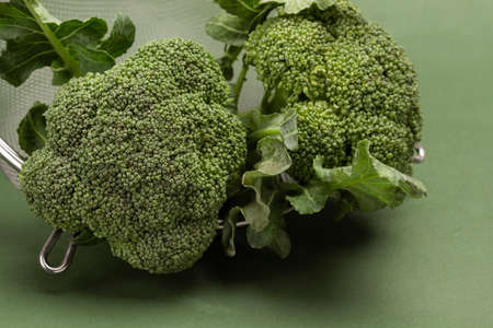 Broccoli in metal colander. close up. top view. green background.の写真素材