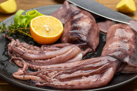 Fresh squid with tentacles, lemon and knife on black plate. close up. top view