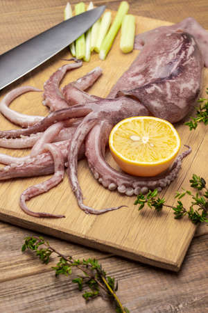 Raw squid with tentacles, lemon and knife on cutting board. top view. wooden backgroundの写真素材